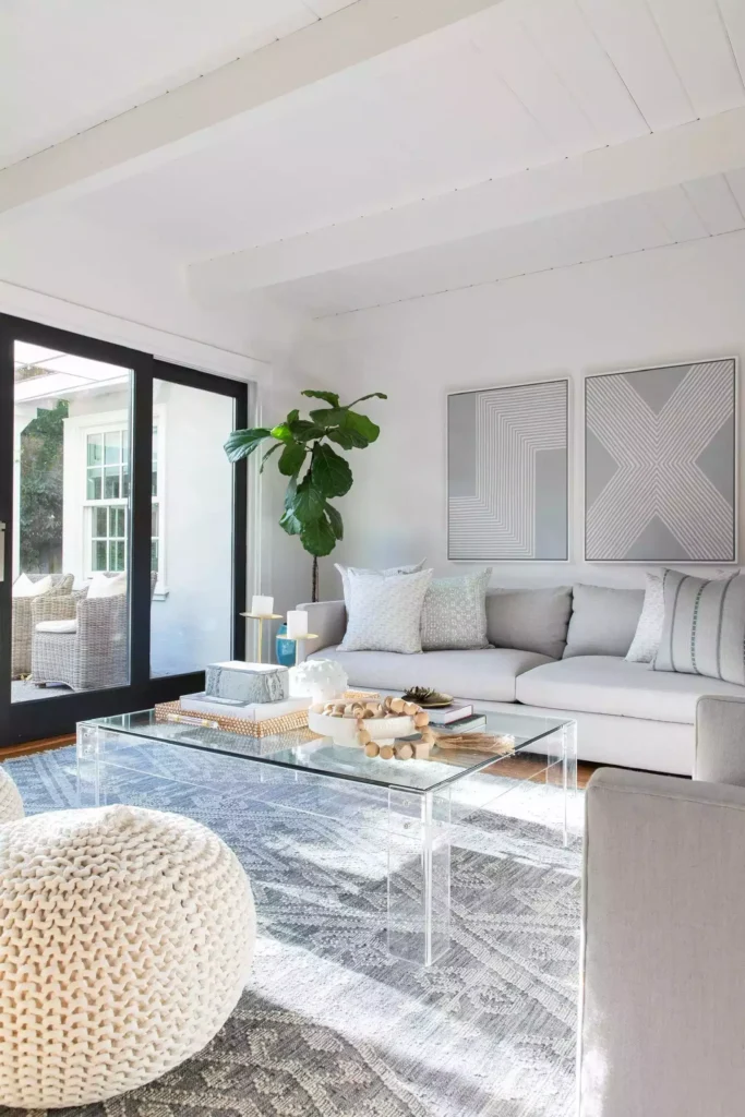 All-white beamed living room, acrylic table, geometric art, knit pouf