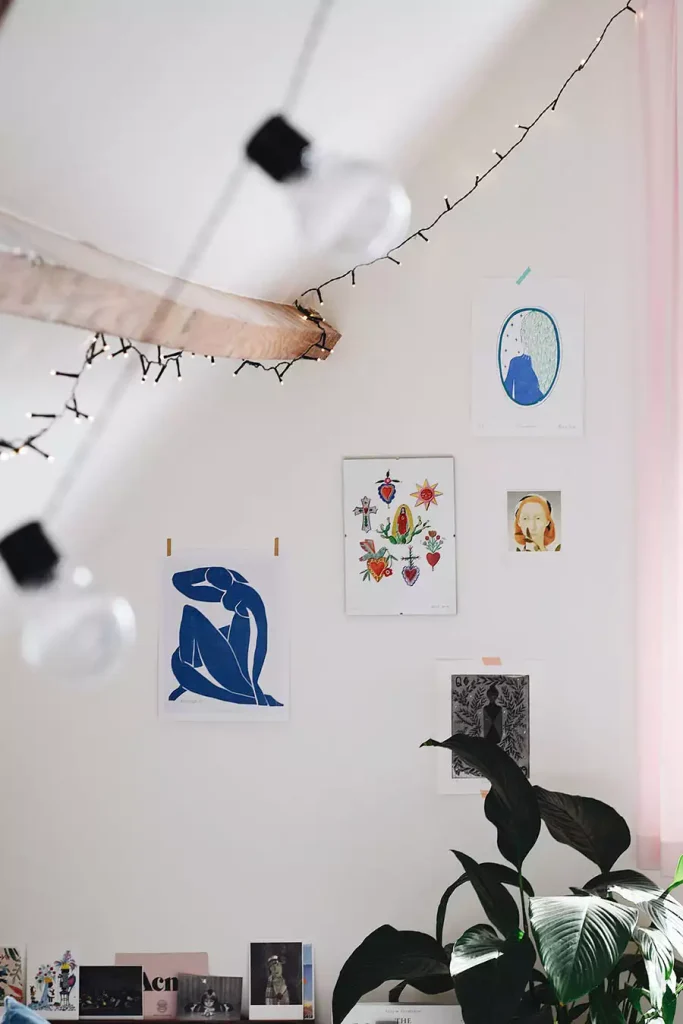Art prints hung on a white wall beneath string lights and a wood beam for easy aesthetic DIY room decor