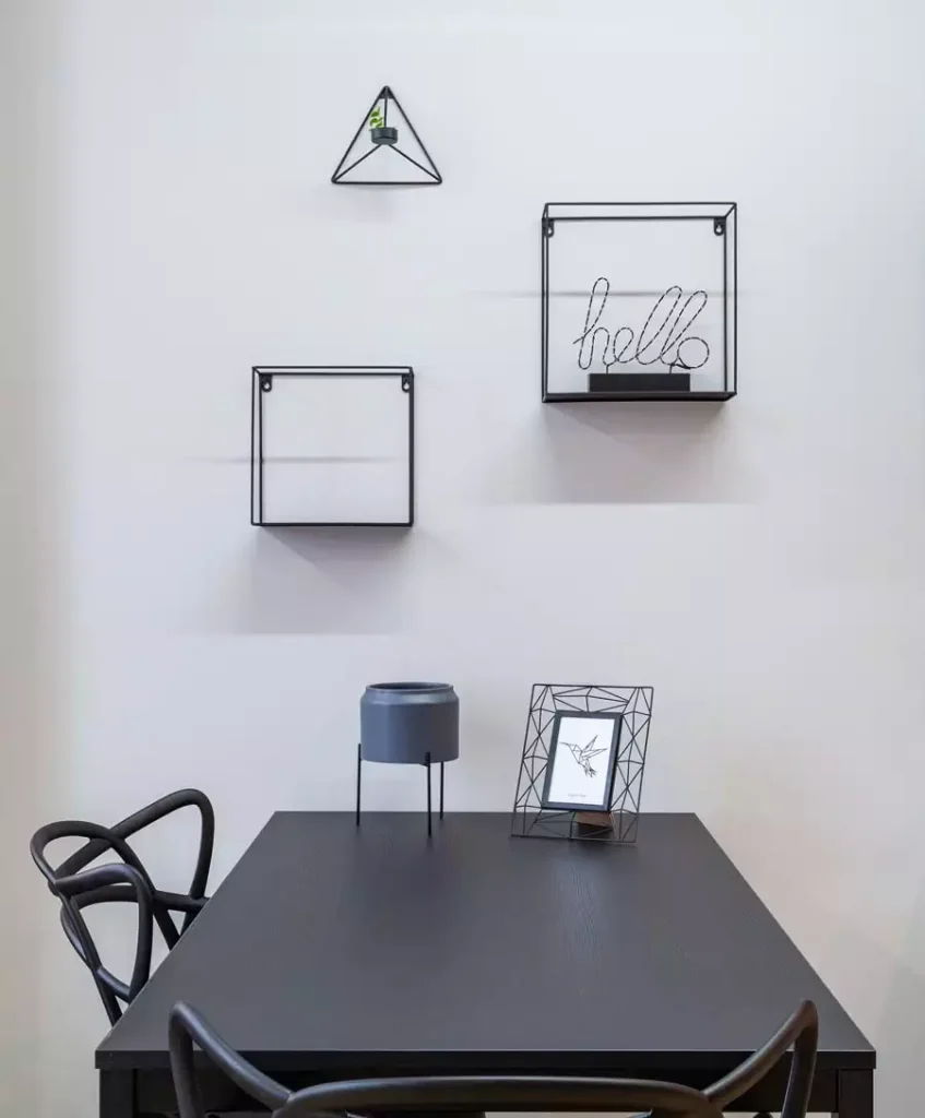 Black Geometric Wire Shelves With A Hello Sign And A Tiny Plant Make Minimalist Dining Wall Decor Above A Black Table