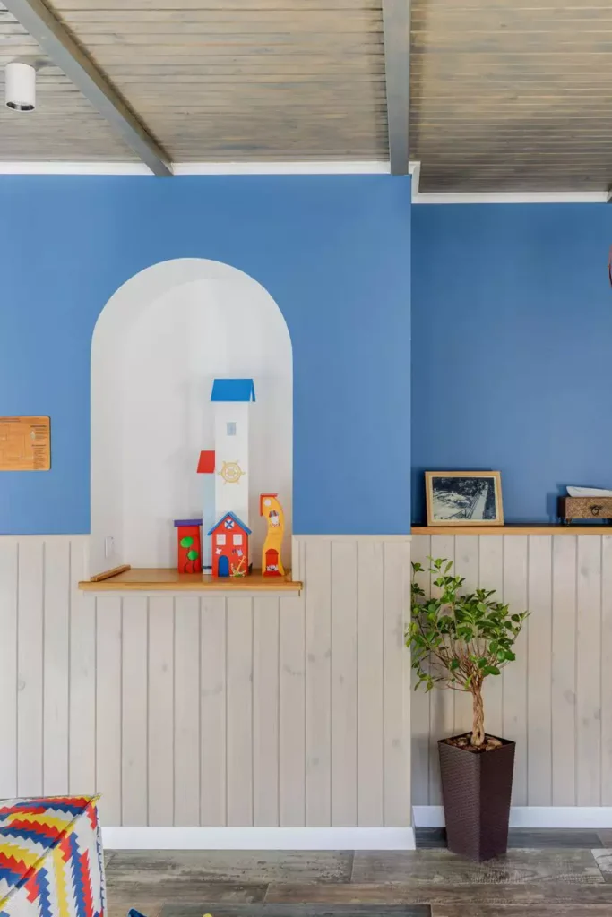 Blue Accent Wall With A White Wall Arch Displaying Wooden Toy Houses