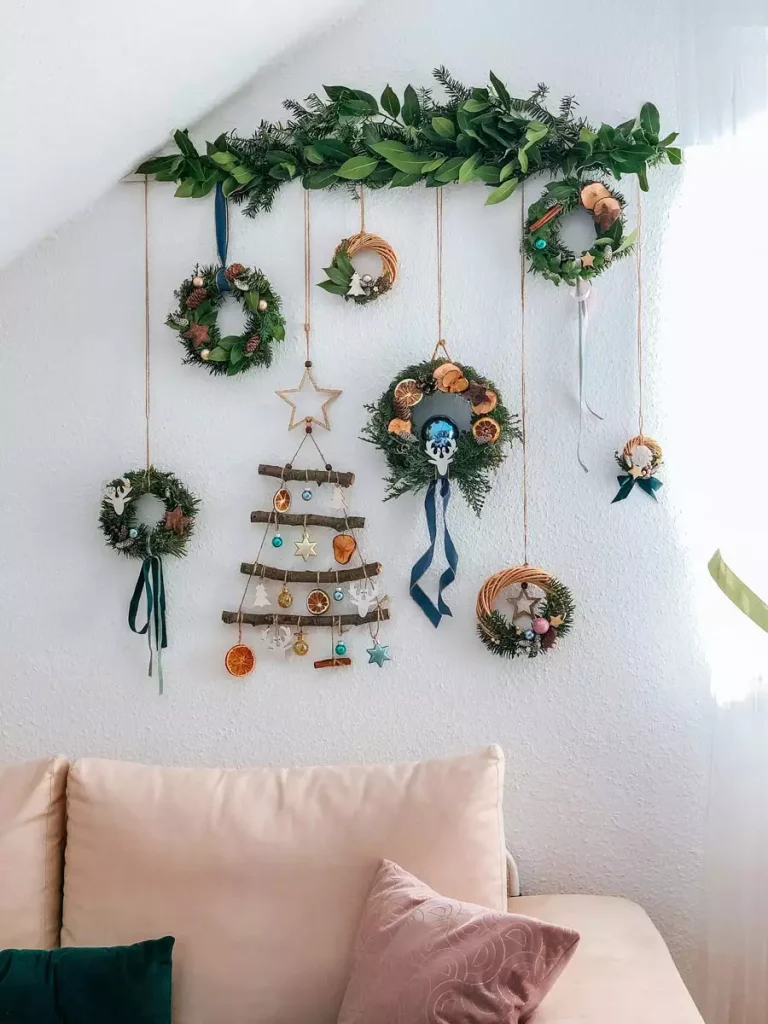 Boho Christmas Wall Display Of Mini Wreaths, A Garland, And Dried-Orange Ornaments Above A Sofa