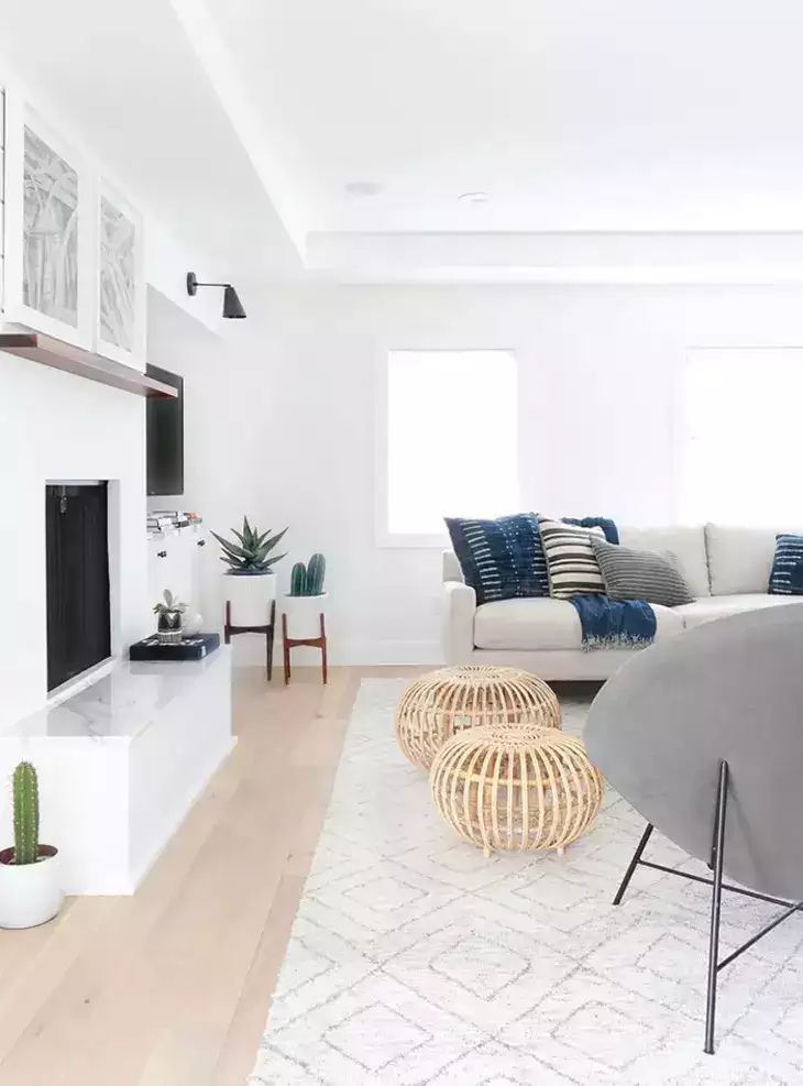 Bright white living room, rattan ottomans, marble hearth, cactus pots, linen sofa