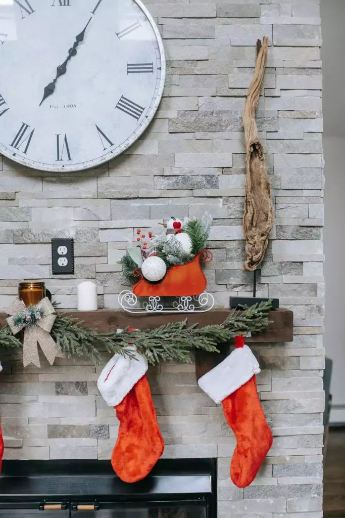 Close-Up Of A Stacked-Stone Christmas Wall Fireplace With A Round Clock And Red Stockings