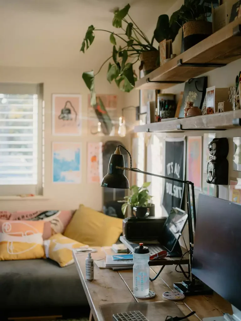 Cozy home office nook room decor with wooden desk, black task lamp, yellow pillows and hanging monstera plants