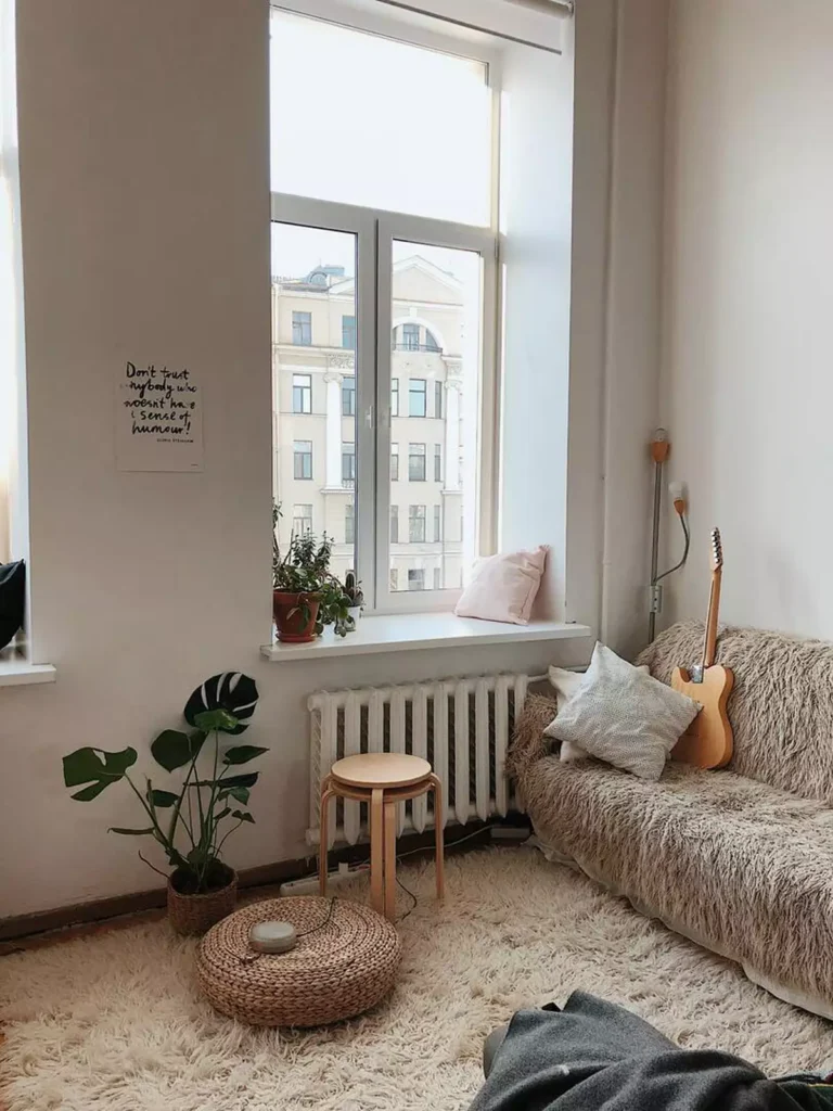 Cozy tan wall living room corner with a fluffy cream sofa throw, guitar, and monstera plant