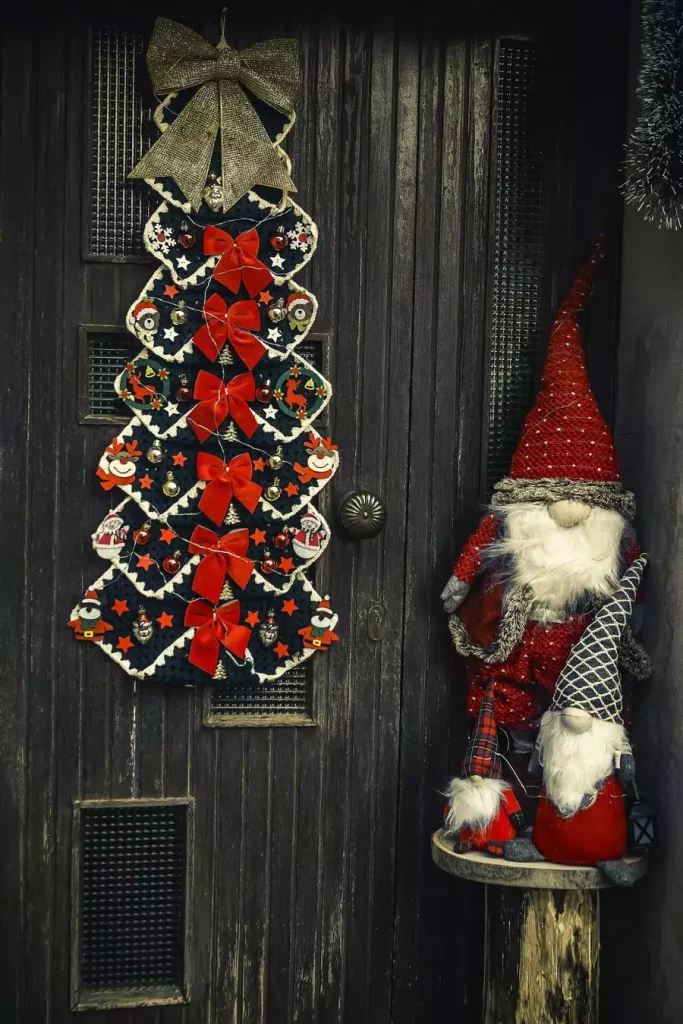 Crocheted Christmas Wall Tree Hanging With Red Bows Beside Gnome Figures On A Rustic Wood Door