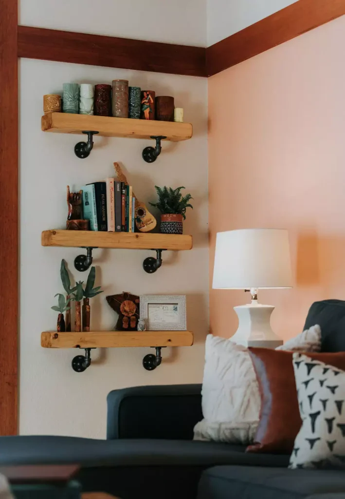 DIY corner wall decor featuring industrial pipe floating shelves displaying tiki mugs and books in a living room corner