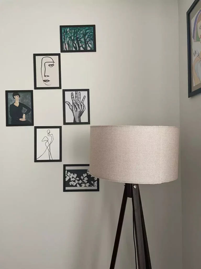 DIY corner wall decor with black framed gallery wall arranged diagonally around a tripod floor lamp in a bright corner