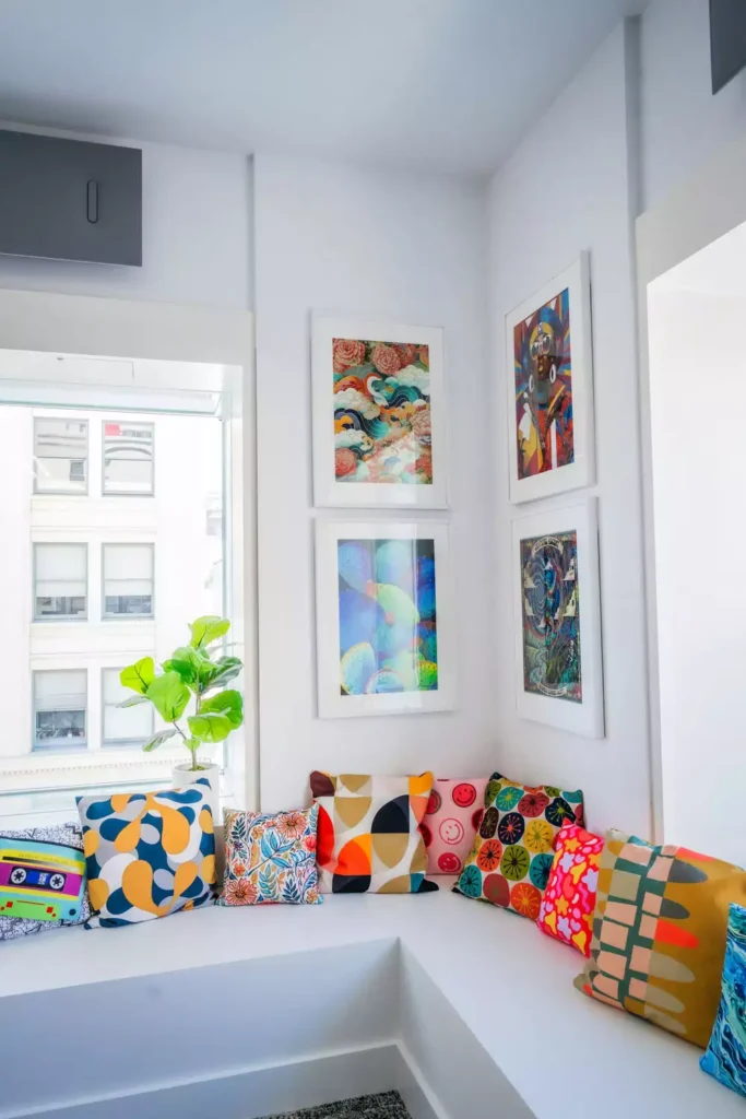 DIY corner wall decor with built-in bench with colorful patterned pillows and four framed art pieces in cozy nook