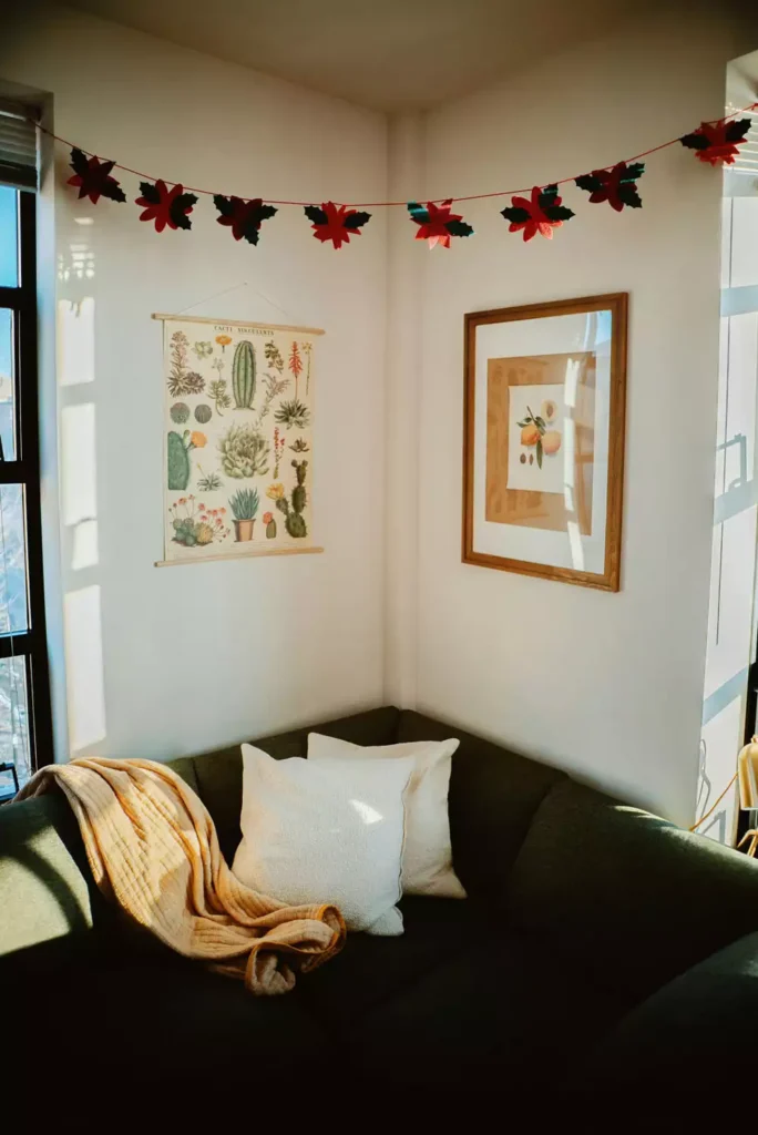 DIY corner wall decor with cactus wall art and poinsettia garland above dark green sectional sofa