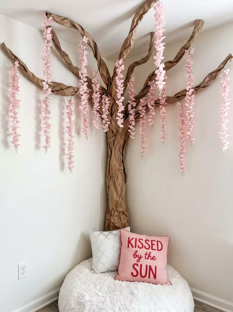 DIY corner wall decor with handmade paper tree with pink blossom branches in cozy reading corner with pouf