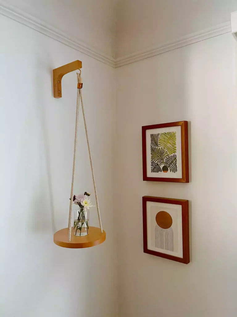 DIY corner wall decor with hanging round shelf displaying flowers and framed floral prints in bright corner