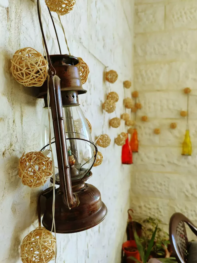 DIY corner wall decor with vintage lantern and rattan ball string lights with colorful glass bottles display on stone wall