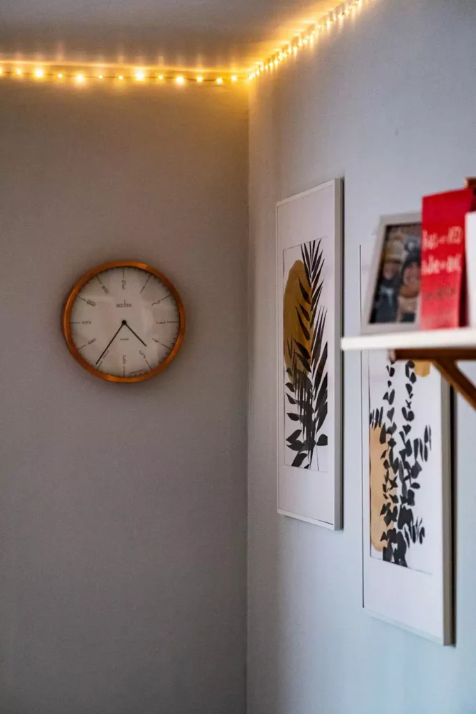 DIY corner wall decor with wooden wall clock and tall botanical prints under warm fairy lights in a cozy corner