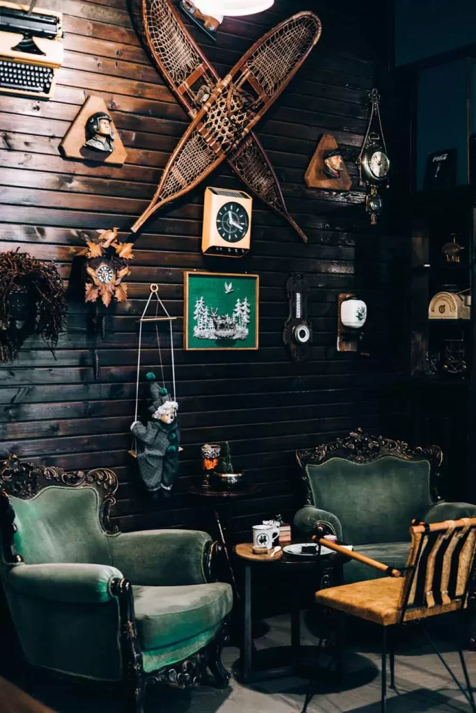 Dark Wood-Paneled Wall Crowded With Crossed Vintage Snowshoes, A Cuckoo Clock, Wall Clocks, And Carved Wooden Bust Ornaments In A Lodge-Style Room