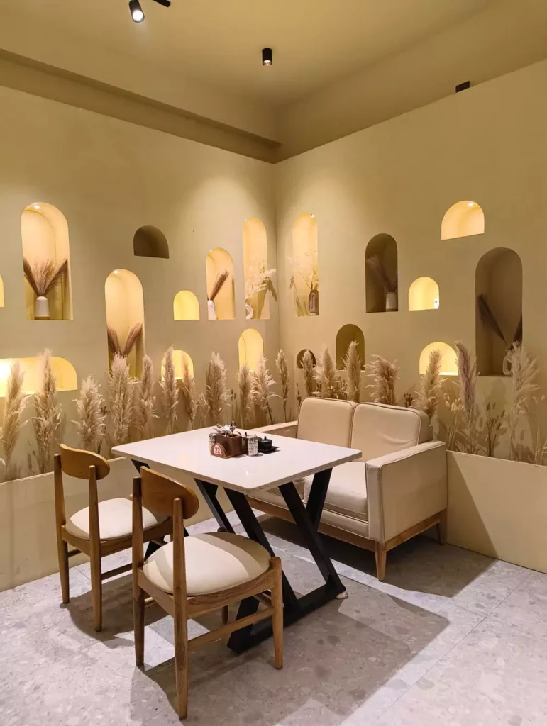 Dining Nook With Wall Arches Filled With Pampas Grass Between Soft Yellow Walls