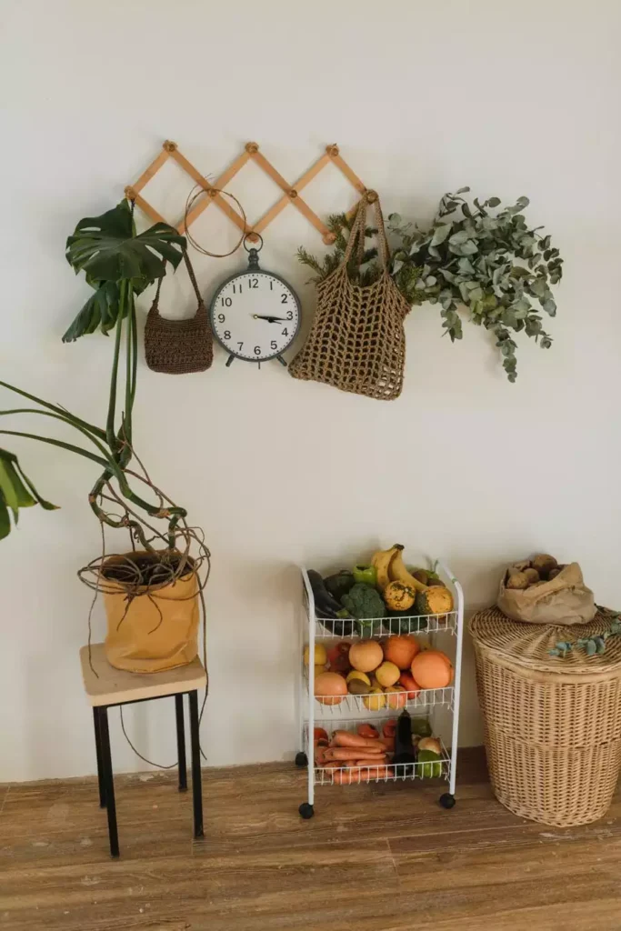 Expandable Wall Peg Rack With A Clock And Woven Bags Adds Natural Kitchen Wall Decor Beside A Fruit Cart
