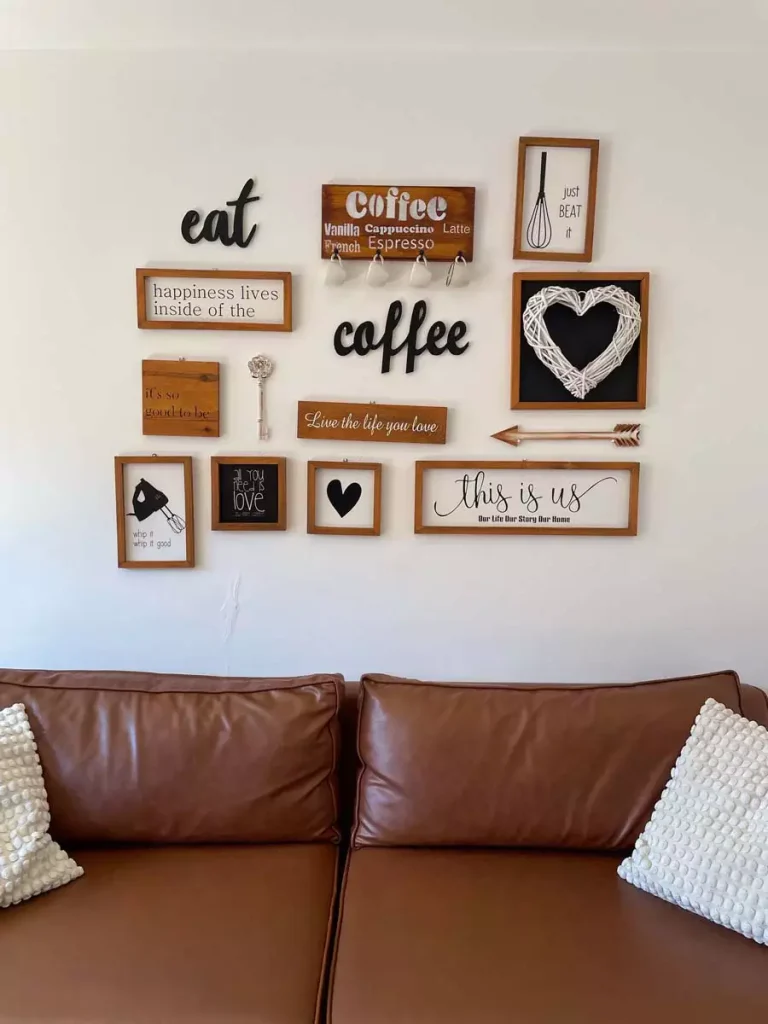 Farmhouse Wall Gallery Of Wooden Kitchen-Themed Sign Art, A Woven Heart Wreath, And A Mini Mug Rack Above A Brown Leather Sofa