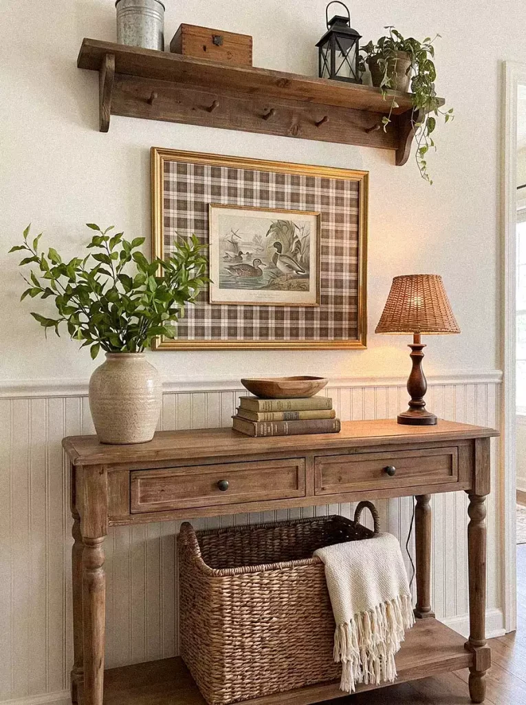 Farmhouse Wall Shelf Holding A Lantern, Tin Pail, And Trailing Plant Above A Plaid-Framed Duck Print, Console Table, And Woven Basket With A Throw Blanket