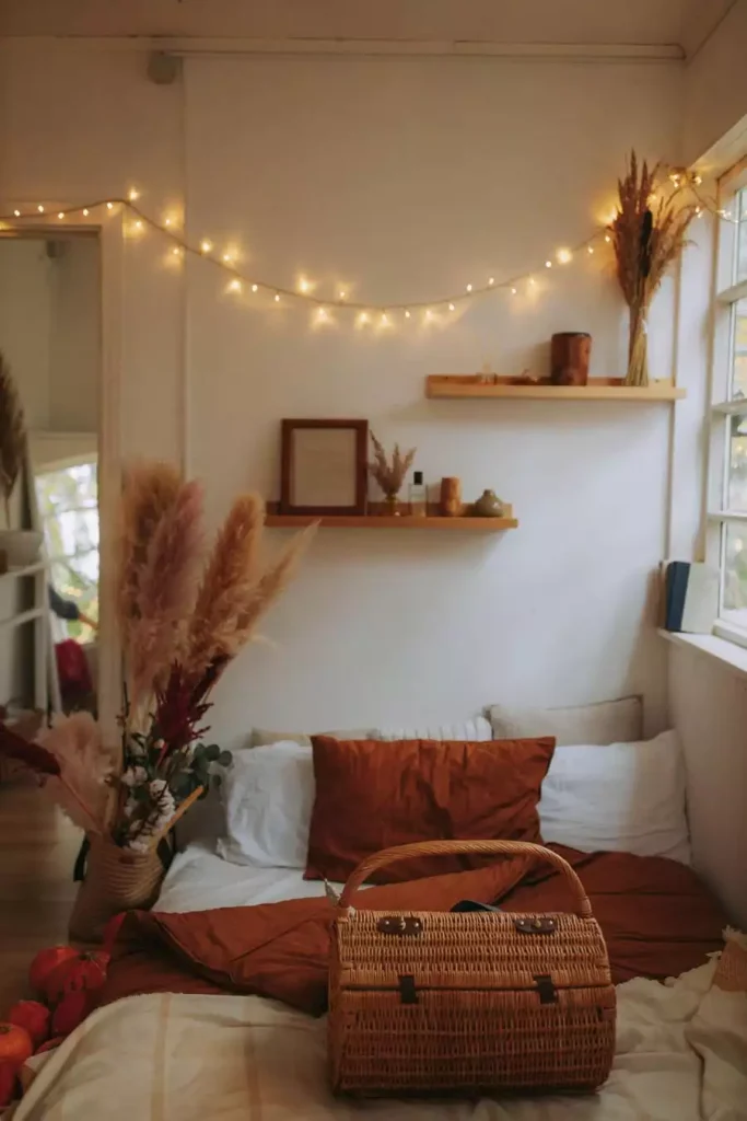 Floating Shelves With Dried Pampas And String Lights Offer Rustic Dorm Wall Decor Above A Rust Colored Bed