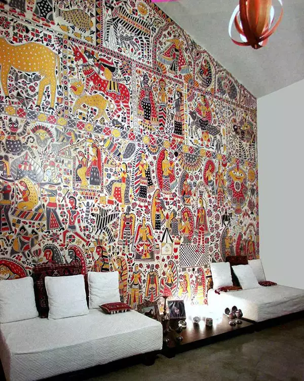 Floor to ceiling Madhubani mural, bold Indian wall decor artwork behind a white low seating living room