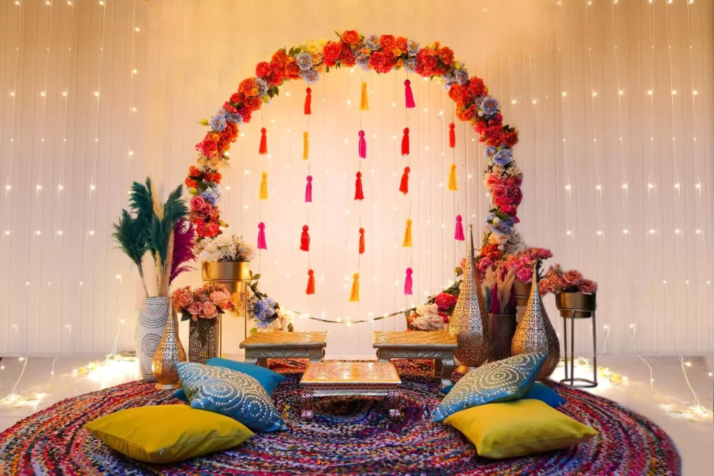 Floral mandap arch with hanging tassels, fairy lights, and Indian wall decor accents styled for a mehndi or festive event