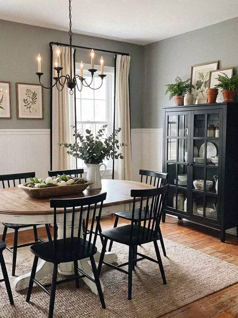 Framed botanical prints on a sage green wall add classic Dining Wall Decor beside a black glass cabinet and round table