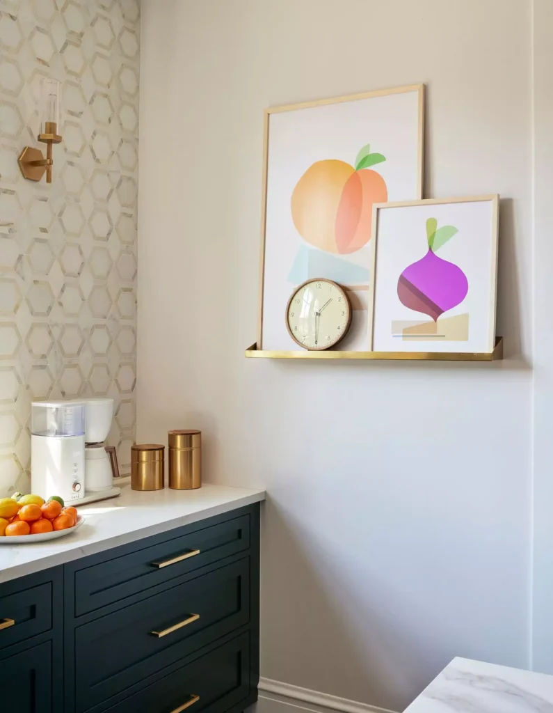 Fruit prints and a small clock on a brass ledge on a navy kitchen wall