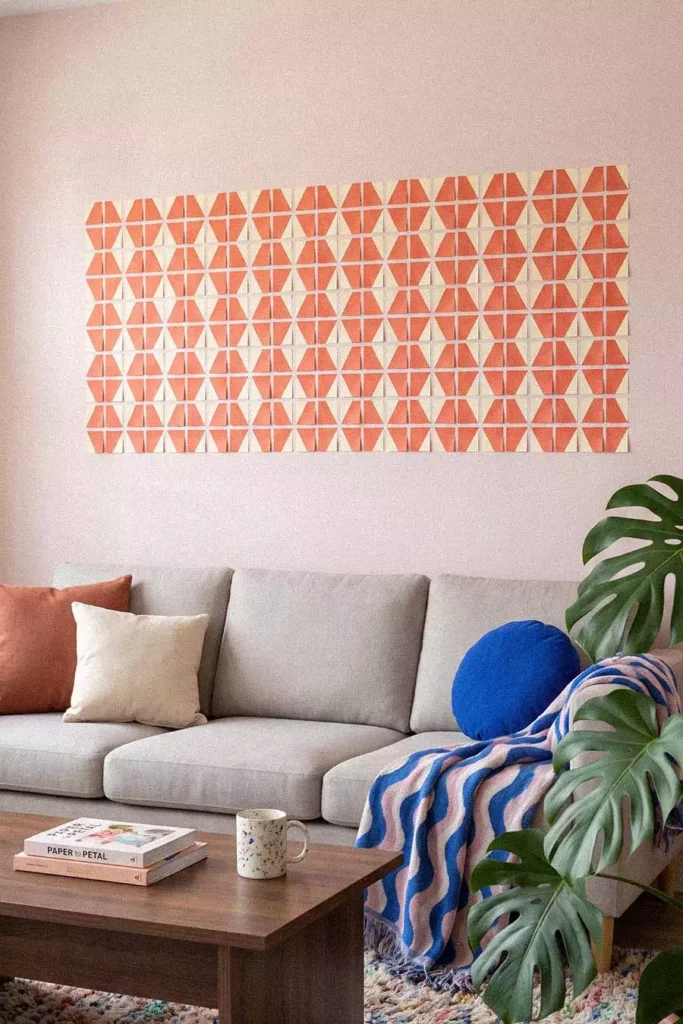 Geometric Sticky Notes Wall Pattern of Orange Triangles on Cream Squares Above a Gray Sofa with a Blue Cushion and Monstera