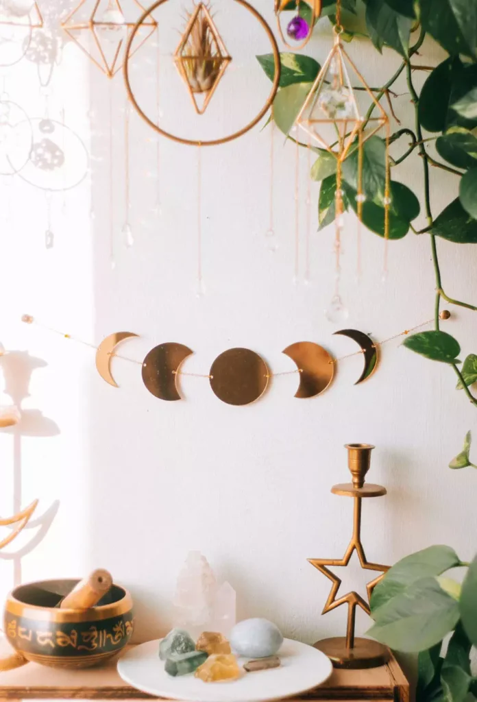 Gold moon-phase garland strung beneath hanging crystal terrariums, celestial wall decor idea