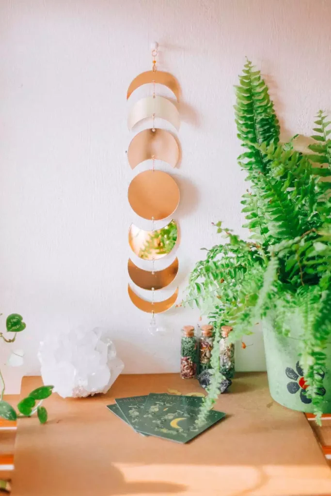 Gold moon phase wall hanging above a wooden table with a crystal cluster and a leafy fern for easy aesthetic DIY room decor