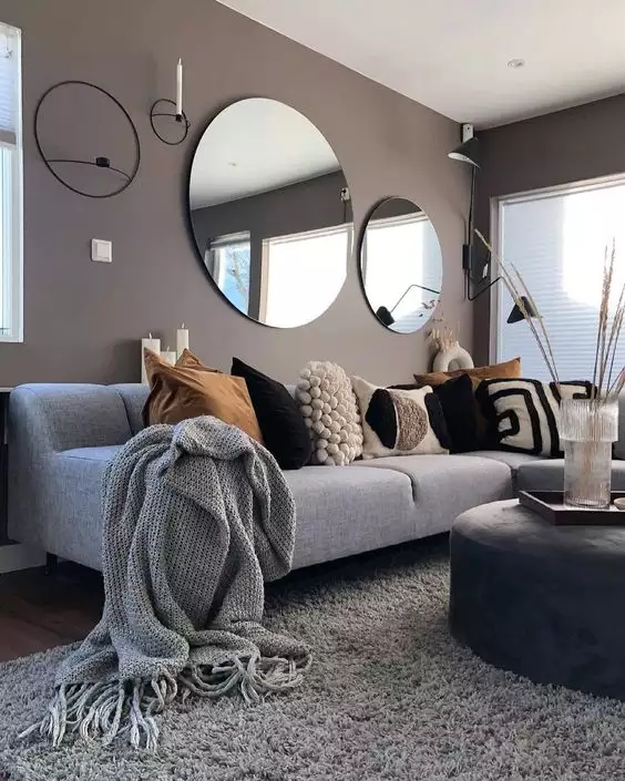 Gray sofa facing two round mirrors on a taupe above sofa wall