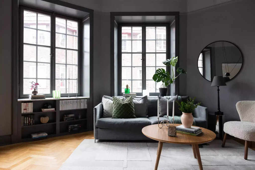 Grey living room decor idea with dark window trim, round mirror and wooden coffee table