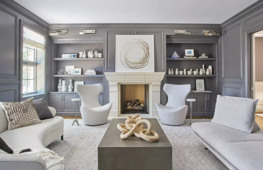 Grey panelled living room walls with built in shelving either side of a white fireplace