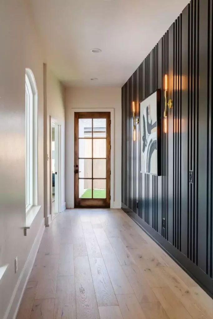 Hallway wall clad in black fluted paneling with brass sconces and abstract art