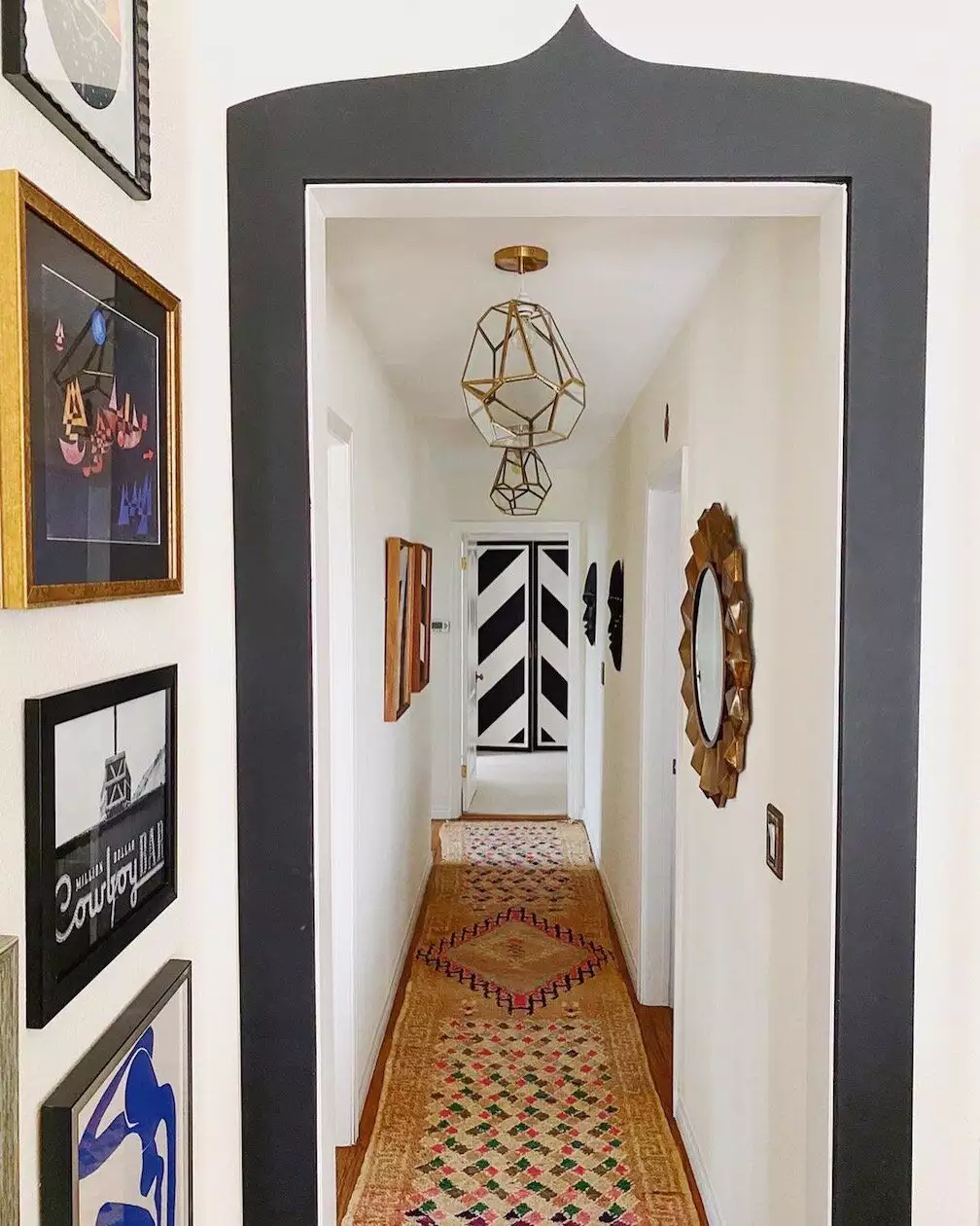 Hallway wall gallery leading to a sunburst mirror and geometric pendant light