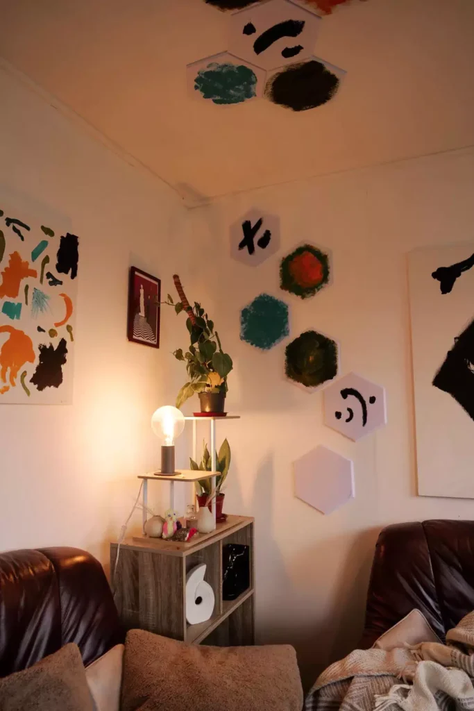 Hand-painted hexagon canvases climbing a corner wall and ceiling, artsy wall decor idea in a cozy leather-sofa nook