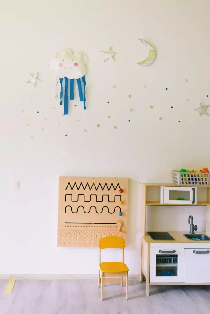 Handmade cloud, moon and star cutouts scattered across a white wall as playful nursery wall decor above a sensory board