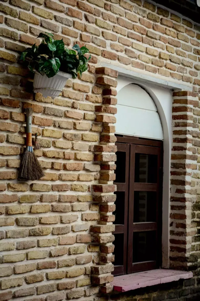 Hanging Planter And Decorative Broom Beside A Brick Archway Door