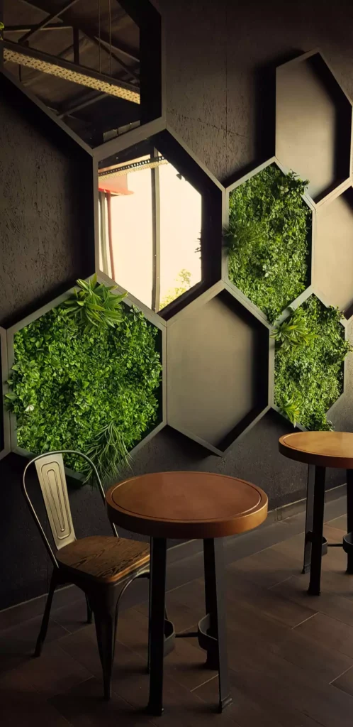 Hexagonal panels filled with greenery and a mirror insert, aesthetic wall decor in a dark café dining space