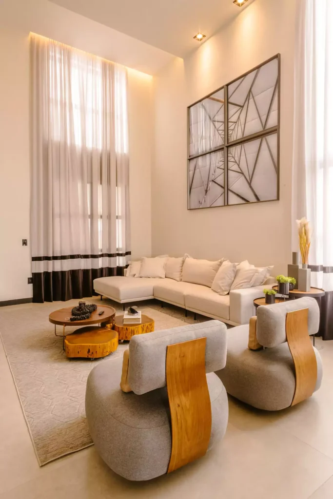 High-ceilinged tan wall living room with floor-length curtains and sculptural wood-and-boucle chairs