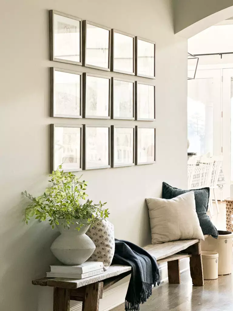 Large wall with a grid of light wood framed mirrors above a rustic bench in a bright living room
