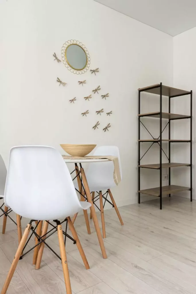 Metal dragonfly accents around a round rattan mirror form delicate Dining Wall Decor in a white dining corner