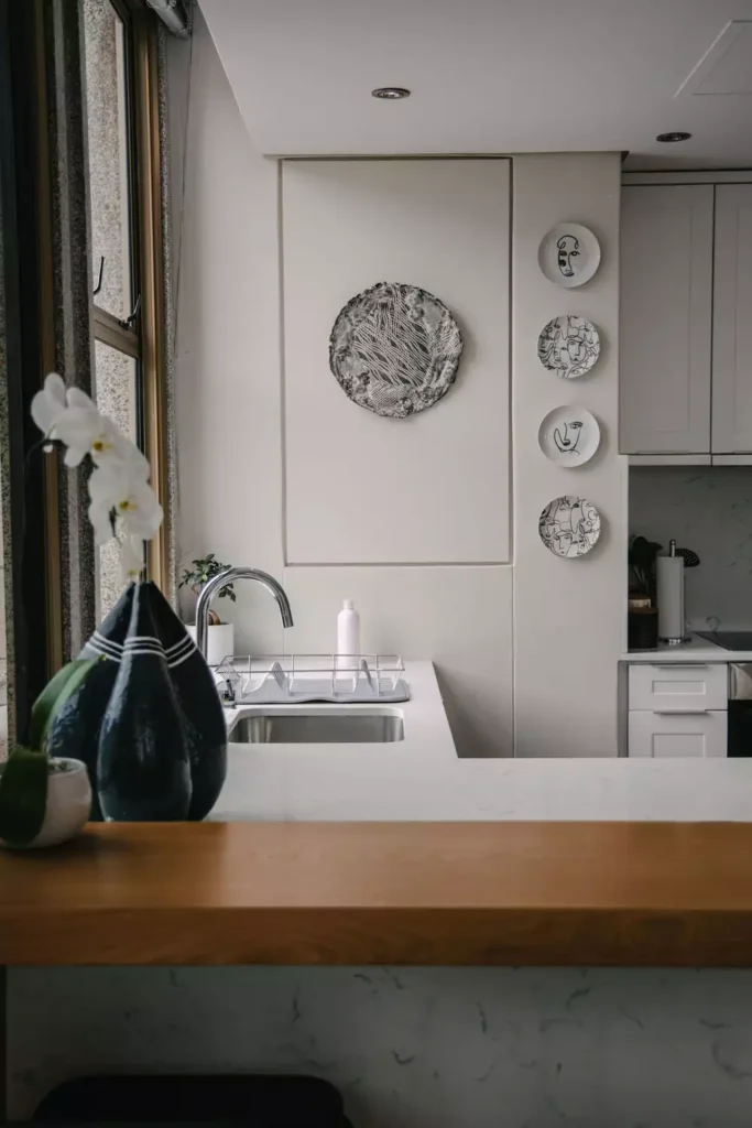 Minimalist face-line plate wall decor beside an abstract metallic disc in a kitchen