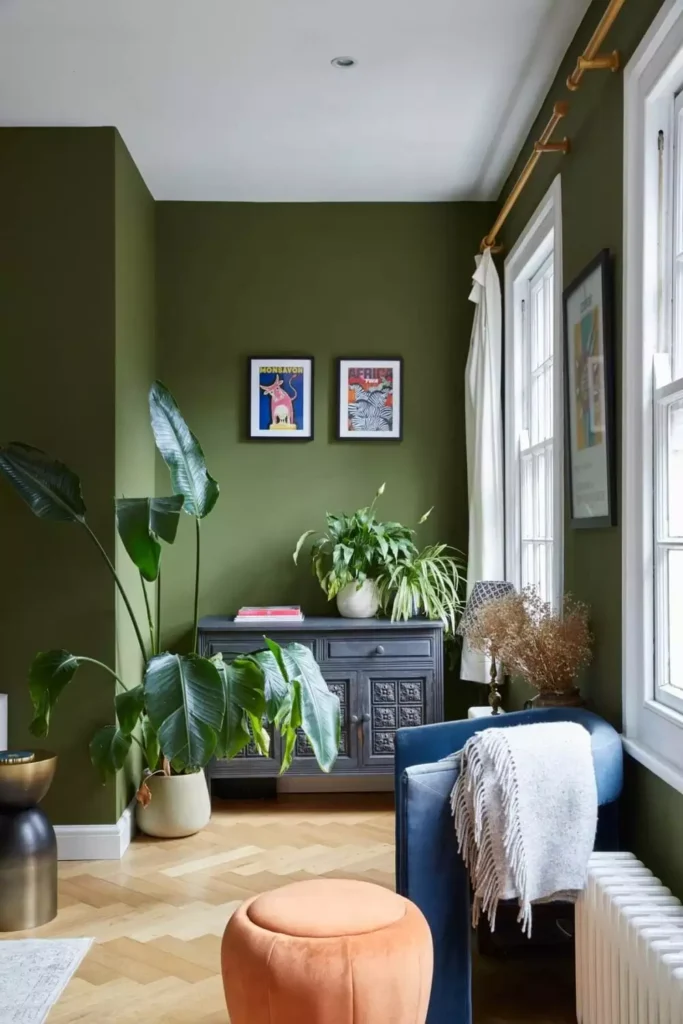 Olive green walls with a blue armchair, large plants, and a dark carved cabinet