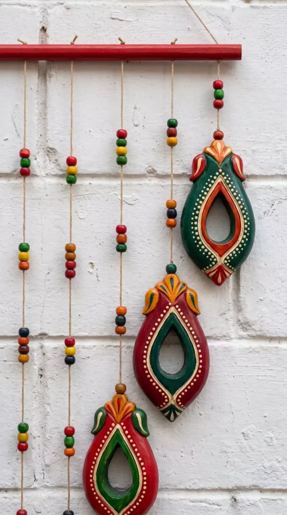 Painted wooden teardrop ornaments on beaded strings, rustic Diwali wall decor on brick