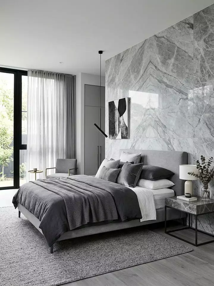 Polished grey marble slab bedroom wall with abstract wall art above a dark grey tufted bed