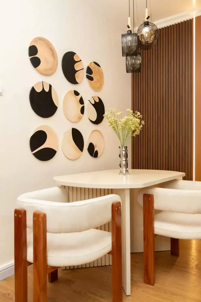 Round black and tan ceramic discs arranged on the wall create artistic Dining Wall Decor above a curved white dining table