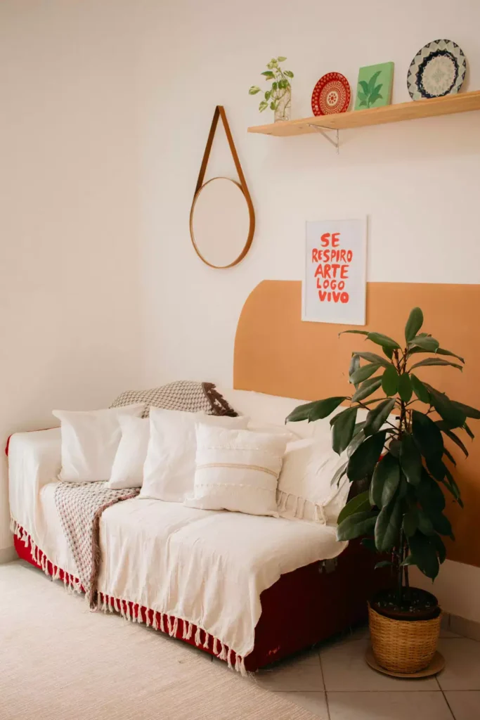 Round leather-strap mirror and a shelf of decorative plates, wall decor idea above a fringed daybed