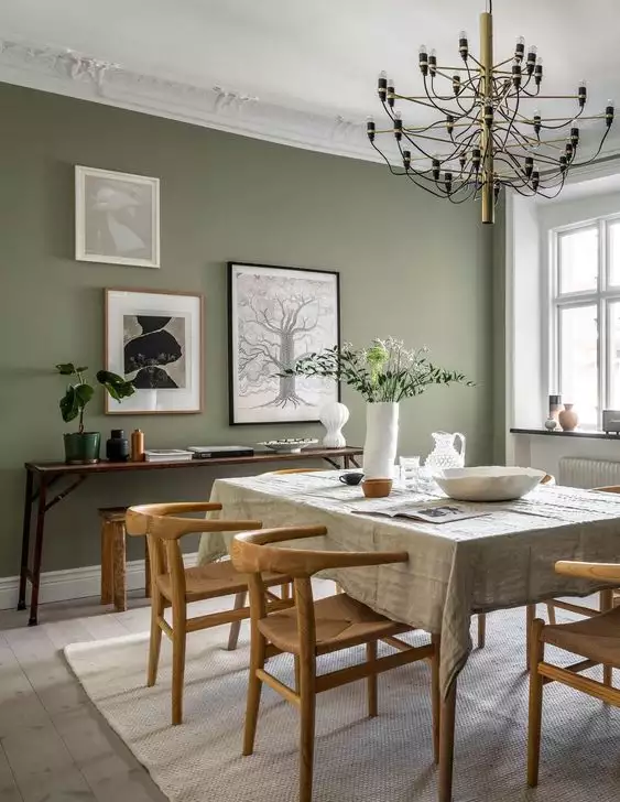 Sage green walls in a dining room with oak chairs, linen table, and gallery art